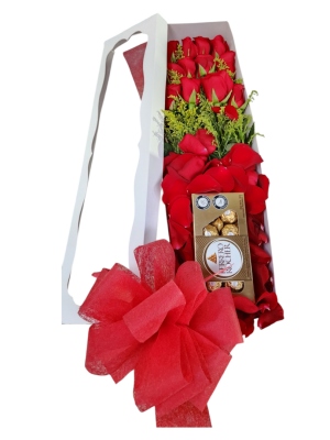Caja blanca con 12 rosas rojas, follaje, pétalos, chocolates Ferrero y moño, un detalle elegante y romántico.